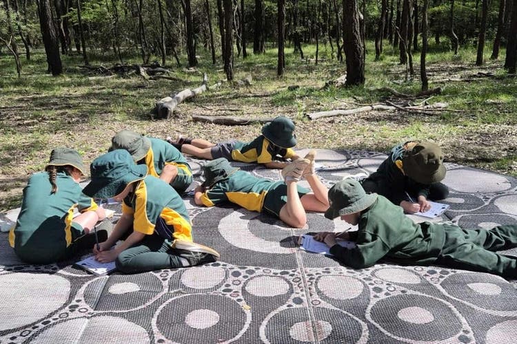 Students completing worksheet questions on a mat in the bush