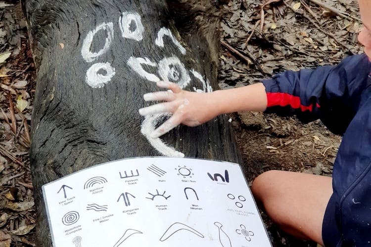 A student painting symbols on a log using ochre