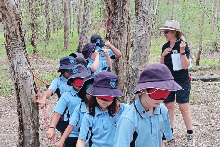 A teacher guiding blindfolded students through the bush